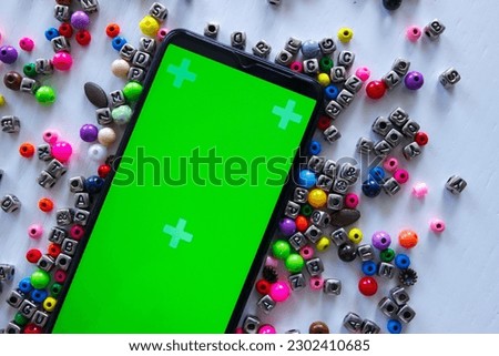 Smartphone with green screen and different colored beads with numbers and symbols, top view