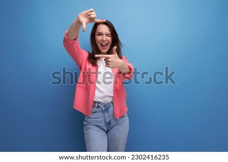 stylish brunette woman in a trendy shirt takes a selfie using a phone on a studio background