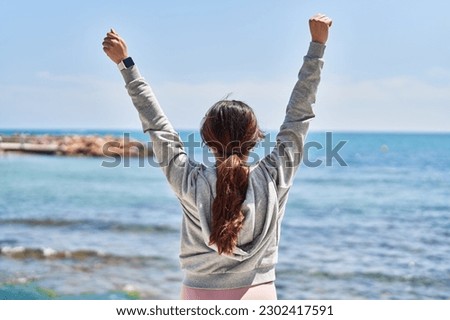 Young hispanic woman standing on back view with arms raised up at seaside Royalty-Free Stock Photo #2302417591