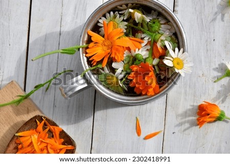 iron mug with flowers and petals of calendula and daisies on a white wooden background, top view