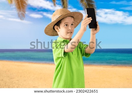 Caucasian little boy smiling making selfie by the smartphone tropical beach background
