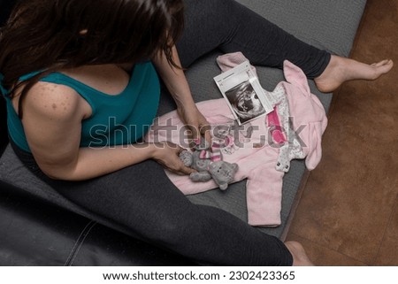 A pregnant girl in a green T-shirt with a toy, an ultrasound picture and a bodysuit