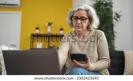 Middle age woman with grey hair using laptop and calculator at home
