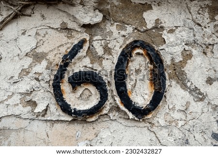 Number 60, black rusty metal on a rendered wall with peeling paint