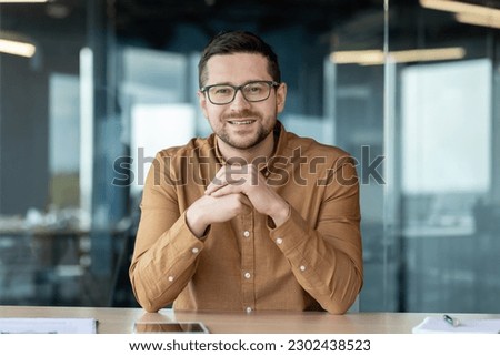 Portrait of a smiling confident man businessman who sits in the office at the table in front of the camera and talks on a video call, conducts business training, consultation. Royalty-Free Stock Photo #2302438523