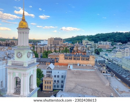 A view of the beautiful town with the clock tower, the river and the hill in the background. The multicolored roofs. Vintage clock on a building in the city of Kyiv. An ancient clock tower in Podol.