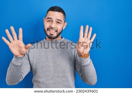 Hispanic man standing over blue background showing and pointing up with fingers number nine while smiling confident and happy. 