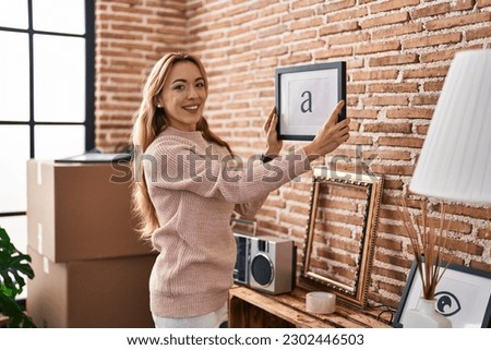 Young woman smiling confident hanging picture on wall at new home