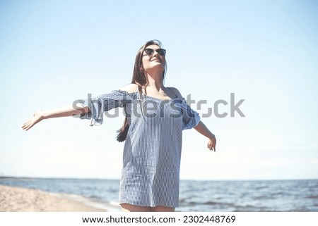 Happy smiling woman in free bliss on ocean beach standing with open hands. Portrait of a brunette female model in summer dress enjoying nature during travel holidays vacation outdoors Royalty-Free Stock Photo #2302448769