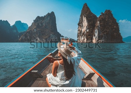 Travel summer vacation concept, Happy solo traveler asian woman with hat relax and sightseeing on Thai longtail boat in Ratchaprapha Dam at Khao Sok National Park, Surat Thani Province, Thailand Royalty-Free Stock Photo #2302449731
