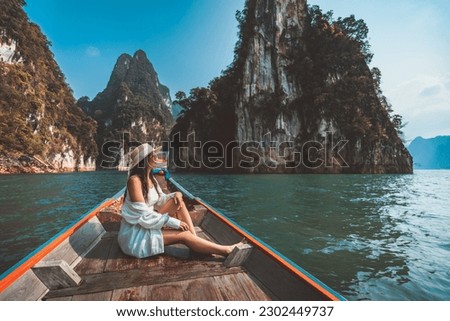 Travel summer vacation concept, Happy solo traveler asian woman with hat relax and sightseeing on Thai longtail boat in Ratchaprapha Dam at Khao Sok National Park, Surat Thani Province, Thailand Royalty-Free Stock Photo #2302449737