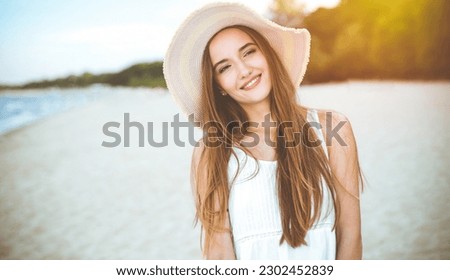 Happy smiling woman in free happiness bliss on ocean beach standing with a hat, sunglasses, and rasing hands. Portrait of a multicultural female model in white summer dress enjoying nature Royalty-Free Stock Photo #2302452839