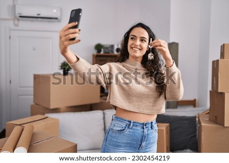 Young hispanic woman make selfie by the smartphone holding key at new home