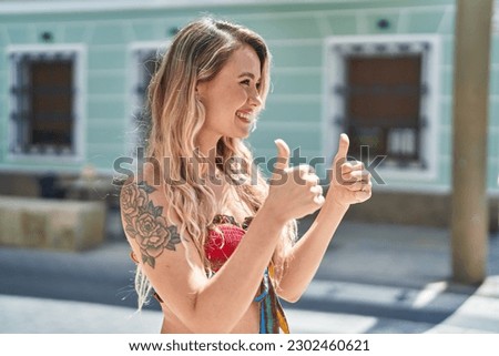 Young blonde woman smiling confident doing ok sign with thumbs up at street