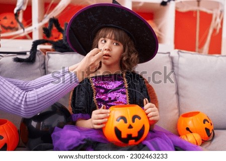 Adorable hispanic girl wearing witch costume having halloween makeup at home