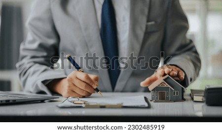 Businessman or real estate agent with house model laying down contract, having contract in place to protect it, signing little agreement form in office, keeping real estate, moving house or renting pr