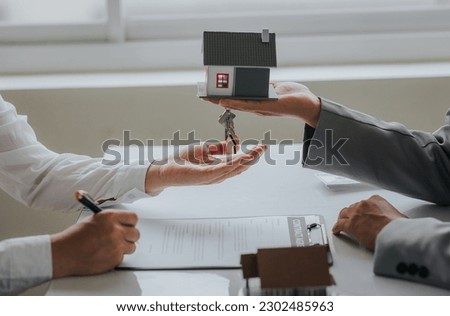 Businessman or real estate agent with house model laying down contract, having contract in place to protect it, signing little agreement form in office, keeping real estate, moving house or renting pr