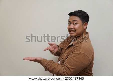 Portrait of young Asian man pointing finger aside empty space isolated over white background.