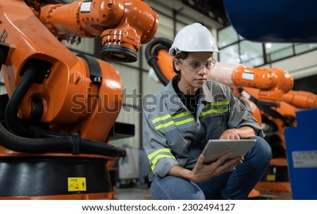 A female engineer installs a program on a robotics arm in a robot warehouse. And test the operation before sending the machine to the customer. Royalty-Free Stock Photo #2302494127
