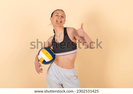 Cute slim brunette girl in sportswear posing with a volleyball. Young athlete with a ball. Isolated on pastel orange, peach background.