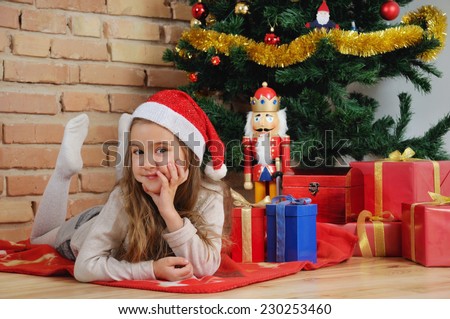 cute little girl lying on the plaid with presents by Christmas tree at home