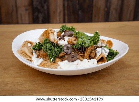 Pasta dish. Closeup view of a plate with pappardelle noodles, pesto, almonds, kale, burrata cheese and tomatoes, in a white dish on the wooden table. 