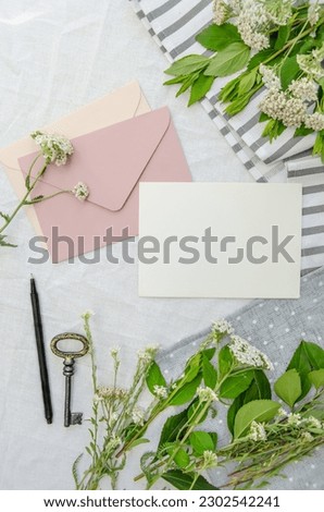 Blank cards and craft rose envelope, vintage key, seasonal herbs on the cotton tablecloth. Creative rustic invitation card, top view.
