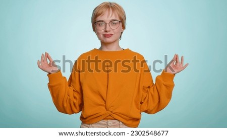 Keep calm down, relax, inner balance. Young woman in glasses breathes deeply with mudra gesture, eyes closed, meditating with concentrated thoughts, peaceful mind. Girl isolated on blue background