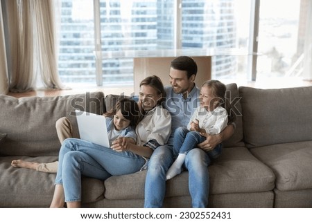 Happy little children and cheerful mother and father watching funny family movie, using learning app on laptop, enjoying leisure time on home couch, using computer, digital gadget for communication