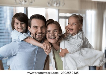 Cheerful young parents piggy backing little kids, holding children, looking at camera with toothy smile, promoting white healthy teeth, dental care, dentistry service