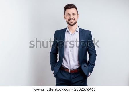 Image of happy brunette man wearing suit smiling at camera with hands in pockets isolated over gray background Royalty-Free Stock Photo #2302576465