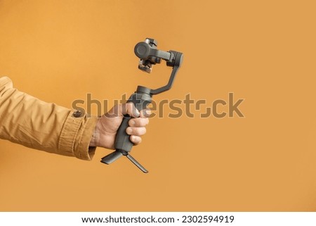 Man hand filming with a smartphone using a gimbal stabilizer on yellow background. Using three-axis electronic stabilizer to make vlogs or video shooting. Copy space for a free text Royalty-Free Stock Photo #2302594919
