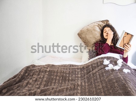 young woman lying crying with photograph and handkerchiefs in bed