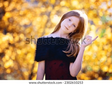 Beautiful young girl with long red hair in red dress outdoors in Fall.