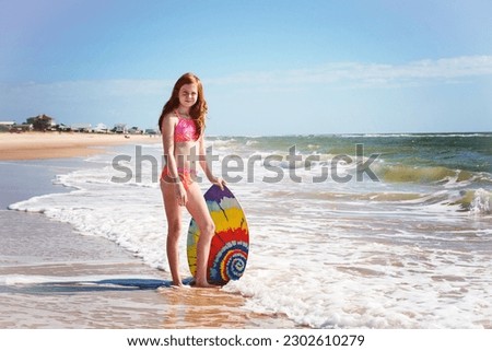 Tween red haired girl in swimsuit with boogie board at the ocean.