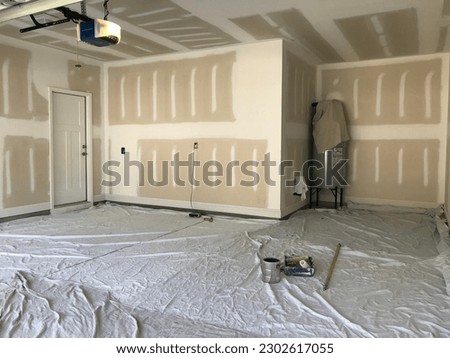 Interior of a garage with raw drywall walls about to be painted. Painters drop cloths are spread out on the floor to keep the paint from getting on the concrete.