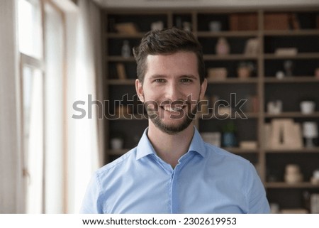 Happy handsome young Caucasian business man head shot portrait. Positive attractive male model with stubble wearing pale blue office shirt, looking at camera with toothy smile