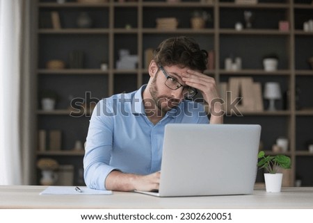 Tired sad freelancer man getting problems with laptop, software error, feeling stress, exhaustion, headache, touching head at home work table, looking at screen with doubt Royalty-Free Stock Photo #2302620051