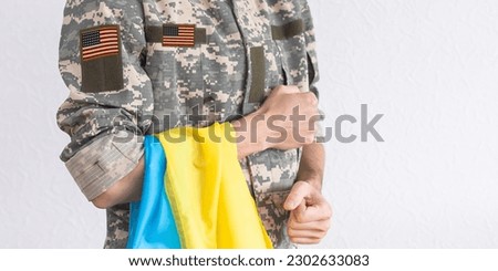 American Flag on Soldiers arm and flag of the Ukraine at background. US military support Ukraine