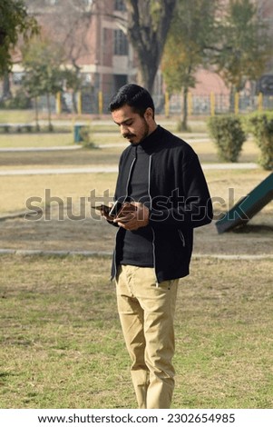 A young man is busy in his mobile phone while standing in a park in Islamabad, Pakistan.