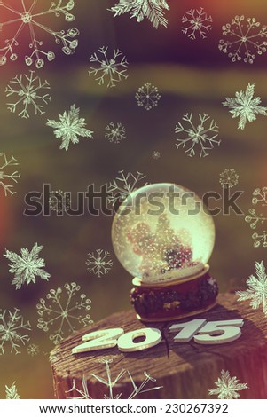 Snow globe with flakes, Christmas tree and a boy and a girl decorating it, placed on a wooden fence with cardboard numbers 2015 on it 