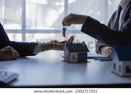 A real estate agent holds a key to a house for his client after signing a concept contract for a business loan, a real estate investment loan, a remote picture.
