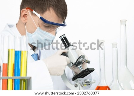 Scientist looking through microscope in laboratory. Virology research and development. Laboratory technician in safety mask and latex gloves. Medicaments and vaccine testing. Pharmacology industry.