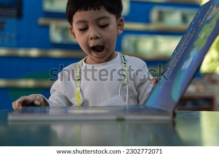 Adorable little Asian child sitting in a book store and reading book with smilling and try to say the words from the pictures in the book. Education, Knowledge concept.