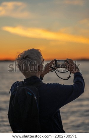 a woman taking a photo at sunset with a smartphone