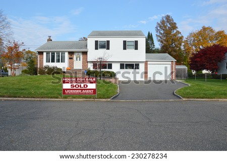 Sold Real Estate (another success let us help you buy sell your next home) sign on front yard lawn of suburban high ranch style home residential neighborhood fall season blue sky clouds USA