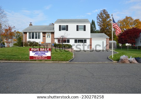 American Flag pole For Sale Real Estate sign on front yard lawn of suburban high ranch style home residential neighborhood fall season blue sky clouds USA