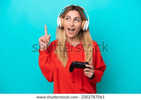 Young Uruguayan woman playing with a video game controller isolated on blue thinking an idea pointing the finger up