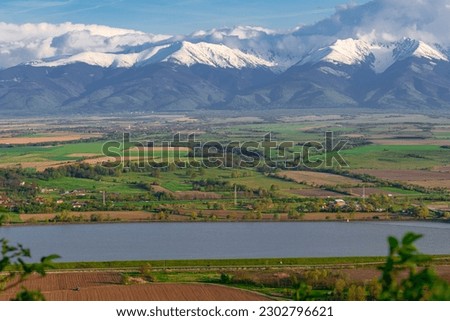 Photography of the beautiful Transylvanian landscape with countryside crops, lake and Fagaras mountains in the background. Photography was taken from a higher ground using a telephoto lens.