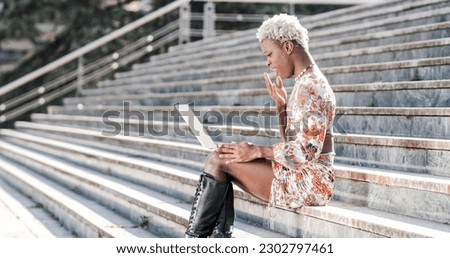 Transgender woman sitting on exterior steps using a laptop, remote worker